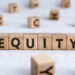 Wooden blocks spelling "EQUITY" are arranged in a row against a light background. Additional blocks with individual letters are scattered around them, subtly emphasizing the concept of equity in an engaging and playful manner. | TitaniumInvest
