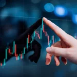 A close-up of a hand pointing at a digital screen displaying a candlestick chart with red and green bars, indicating stock or financial data. The background is blurred with blue hues and light spots, suggesting a busy, high-tech investing environment. | TitaniumInvest